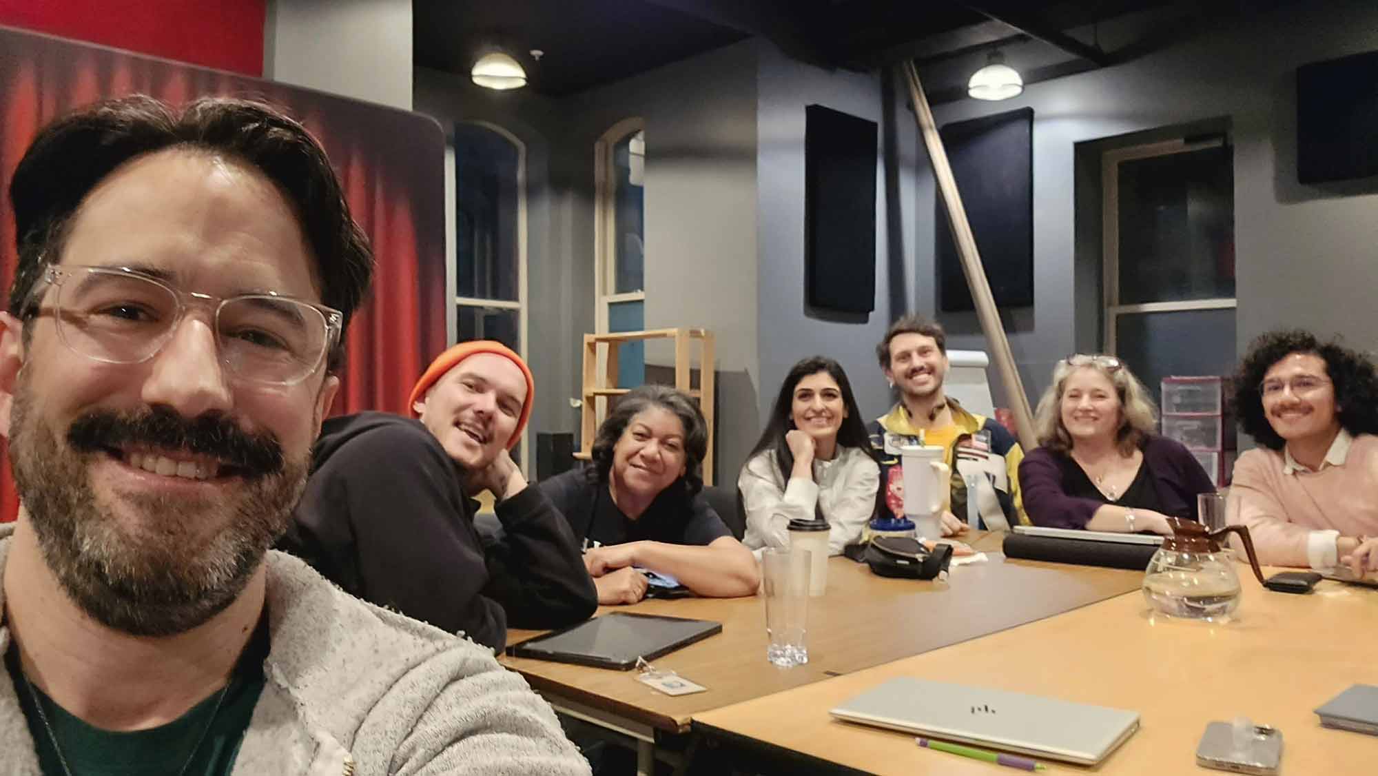Un autoportrait des acteurs et de l’équipe autour d’une table avec des ordinateurs portables.