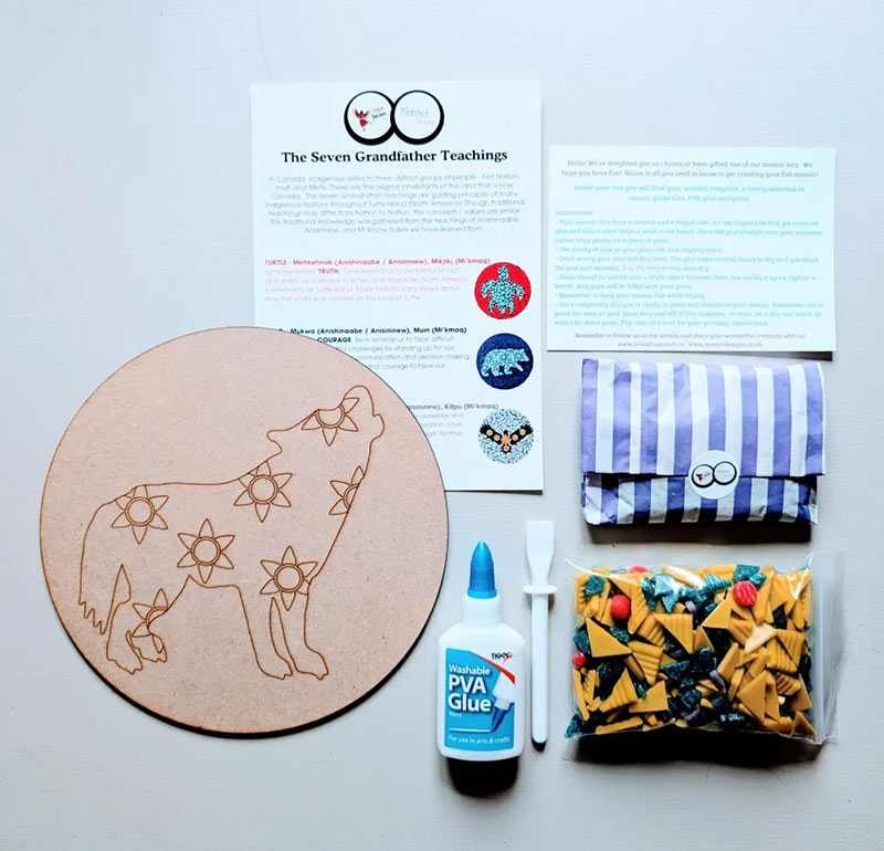 Une trousse de mosaïque posée sur une table, comprenant un gabarit circulaire de loup en bois aux motifs complexes, un sachet de carreaux de verre colorés, de la colle, un outil d’étalement, des cartes d’instructions et une feuille de référence sur les enseignements des Sept Grands-Pères.