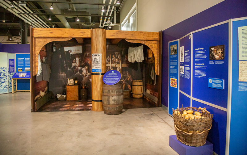 Une salle de maquettes montrant l’intérieur d’un vieux navire, avec plusieurs accessoires et une grande photo de personnes dans des couchettes.