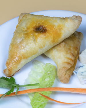 Une assiette blanche contenant deux ukajas dorés, de minces bâtonnets de carottes, une feuille de laitue, un brin de persil et deux tranches de fromage blanc.
