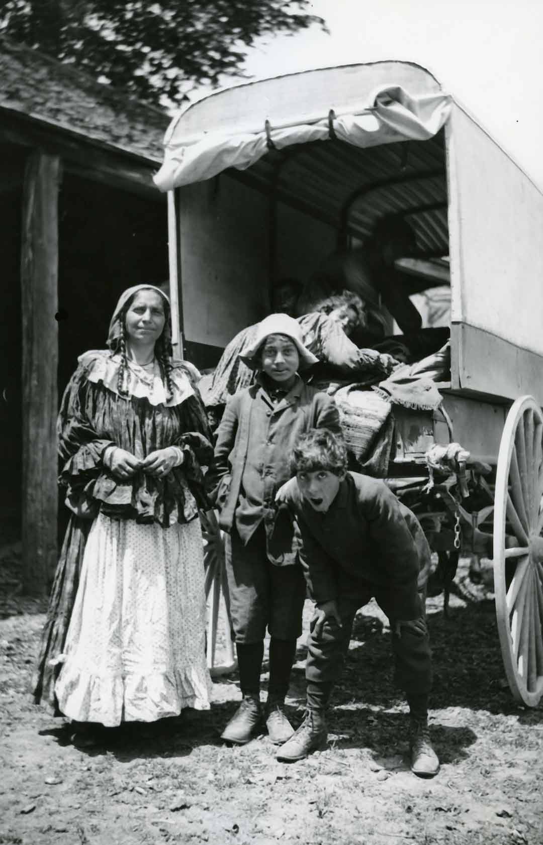 Photographie en noir et blanc d’une femme et de deux enfants souriant devant une caravane.