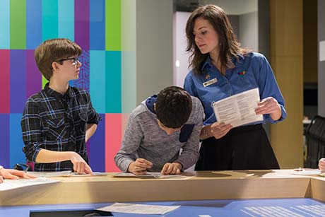 Une interprète regarde deux jeunes garçons qui tentent de remplir un test de citoyenneté canadienne.