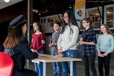 ADes enfants devant une interprète du patrimoine habillée comme une agente d’immigration.