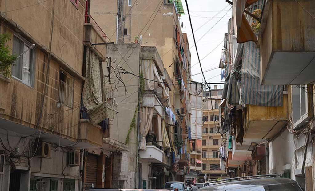Une rue achalandée avec des voitures stationnées de chaque côté. Toutes les maisons ont de la lessive accrochée aux cordes à linge.