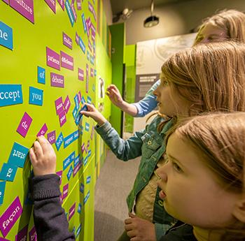 Des jeunes filles composent des phrases sur un mur en assemblant des bandes de mots dotées d'un dos magnétique.