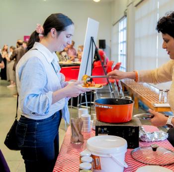 Lors d'un événement organisé au musée, une Indienne vêtue d'un sari sert un curry à une jeune femme d'origine européenne.