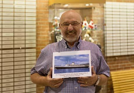 Un homme d'un certain âge tient une photo de navire devant les plaques du Mur d'honneur.