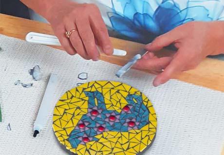 Une mosaïque représentant un ours bleu sur fond jaune, réalisée à partir de morceaux de verre collés sur une assiette ronde.