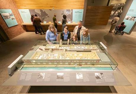 Un guide, un homme et une femme discutent devant la maquette du Pier 21 historique, de la taille d'une table.