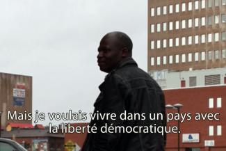 Un jeune homme se tient devant un immeuble et regarde par-dessus son épaule.