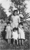 Femme avec trois enfants devant un arbre et un mur de briques.
