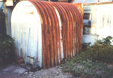 Vieil abri antiaérien rouillé dans le jardin derrière une maison.