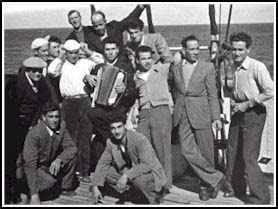 Bruno jouant de l’accordéon au milieu de plusieurs jeunes hommes sur le pont d’un bateau.