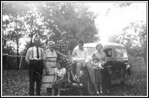 Vieille photographie montrant la famille devant un vieux modèle de voiture.