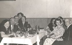 Hommes et femmes de part et d’autre d’une table garnie de bouteilles et de verres.