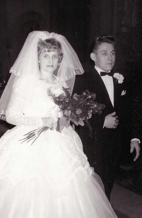 Un couple de mariés lors du jour de leur mariage. La mariée tient un bouquet et porte un voile.
