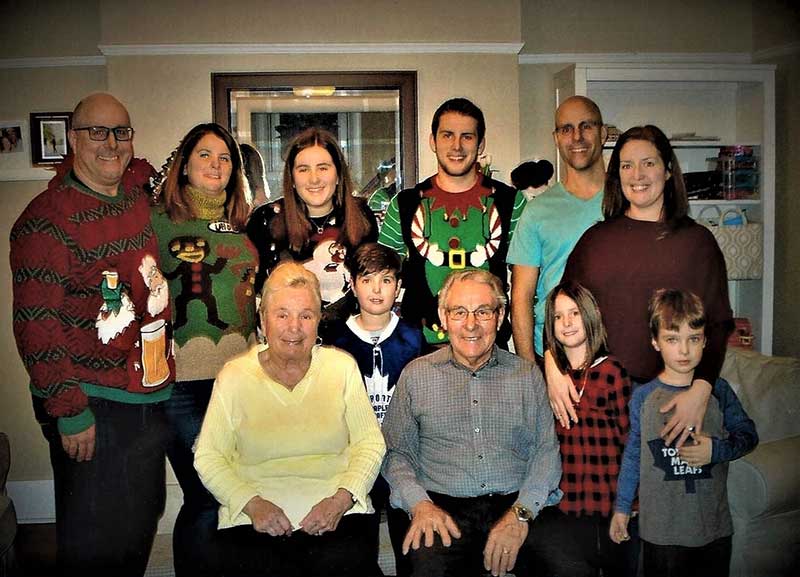 De jeunes membres d’une famille portant des chandails de Noël. Ils sont autour d’un couple âgé qui est assis