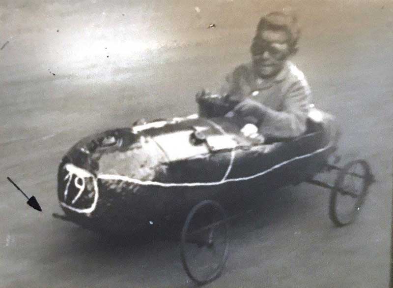 Un petit garçon portant des lunettes. Il est assis et pilote son go-kart.