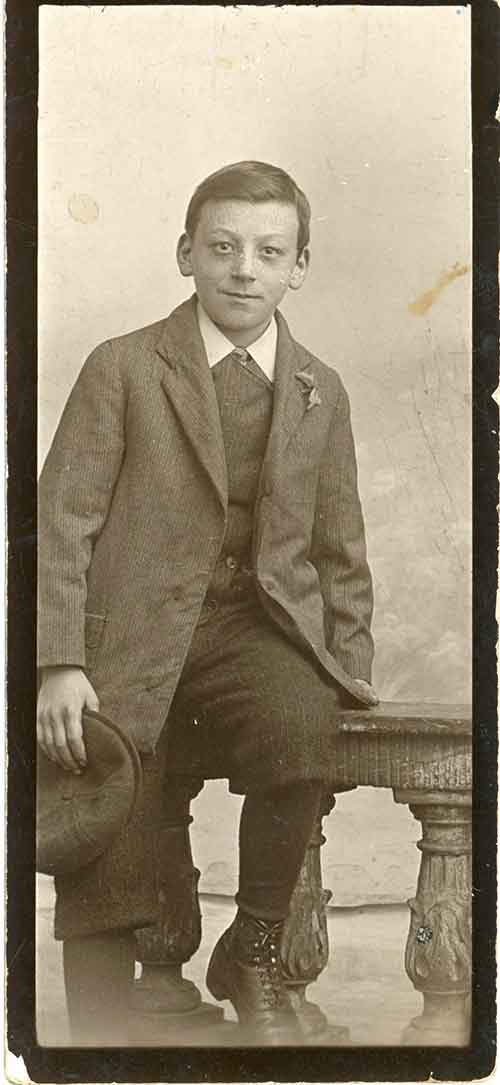 Un jeune homme à moitié assis sur un tabouret. Il porte des vêtements de l’époque.
