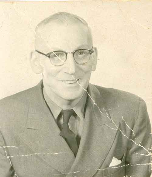 Une vieille photo craquelée d’un homme souriant qui porte des lunettes.