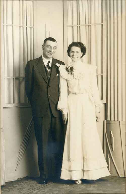 Un couple le jour de leur mariage. Ils sourient joyeusement à la caméra.