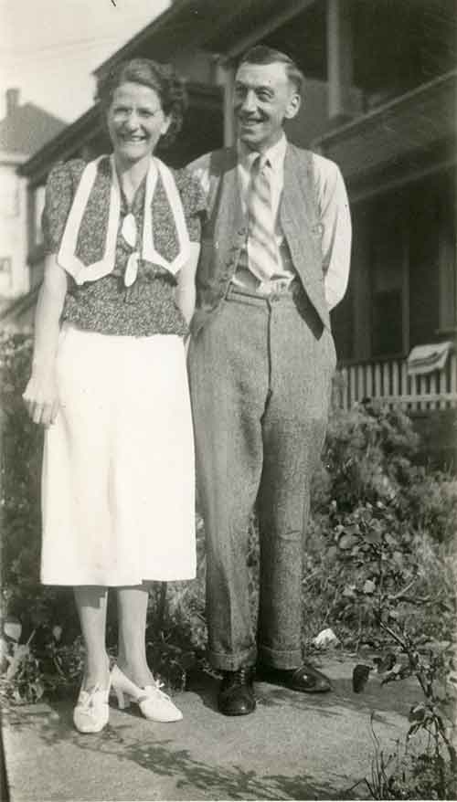 Un couple souriant devant la haie de leur maison.