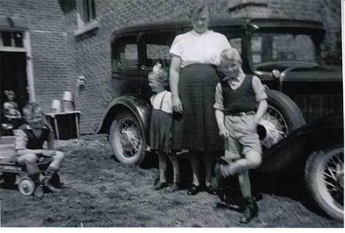 Deux enfants et une femme se tiennent devant une voiture.