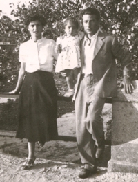 Un homme et une femme debout contre une clôture de pierre, avec une petite fille entre eux.