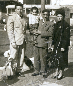 Photo extérieure de deux hommes, une femme en manteau noir et un petit enfant dans les bras de l’homme.