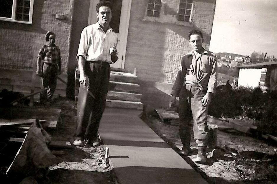 Photo en noir et blanc de trois hommes travaillant sur le ciment marcher à l’extérieur de la maison.