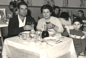 Jeune homme, femme et enfant assis à la table à dîner chargée d’assiettes et de verres.