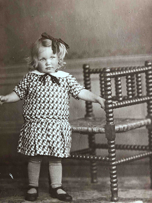 Une petite fille blonde avec un arc dans les cheveux pose pour la caméra.