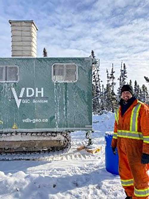 Un jeune homme en équipement de sécurité se tient à côté d’une grande machine pour voyager sur la neige.