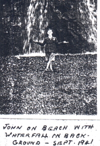 John sur la plage avec cascade en arrière-plan.