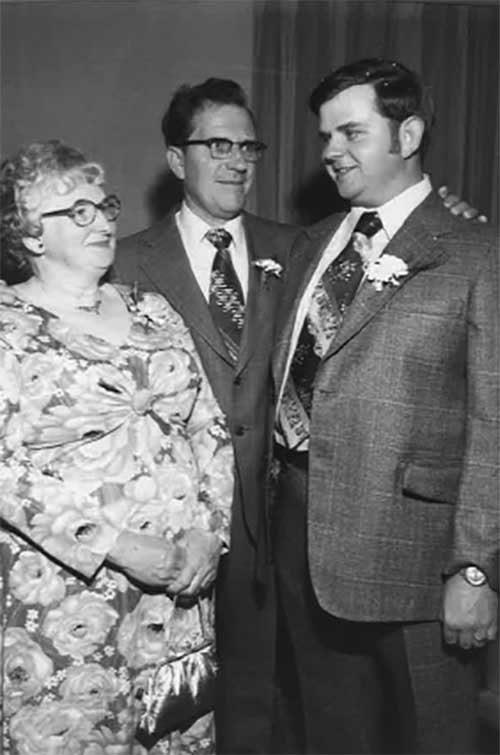Une mère et un père regardent fièrement leur fils à l’occasion de son mariage.