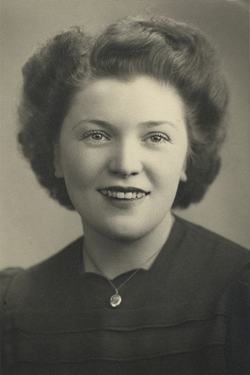 Vieille photo d’une jeune femme aux cheveux bruns courts, elle porte un médaillon.