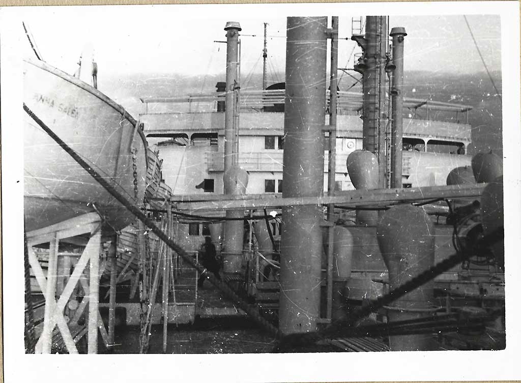 Photo en noir et blanc d’un pont de navire avec un canot de sauvetage à gauche.
