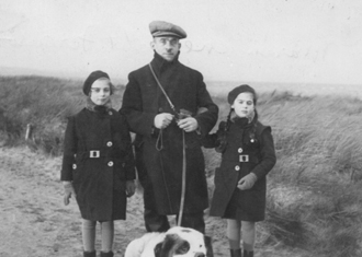 Un chien en laisse, avec une jeune fille de chaque côté.