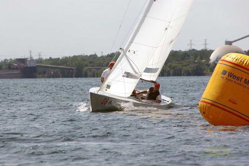 Deux hommes dans un bateau à voiles de course. Ils tournent autour d’une bouée.