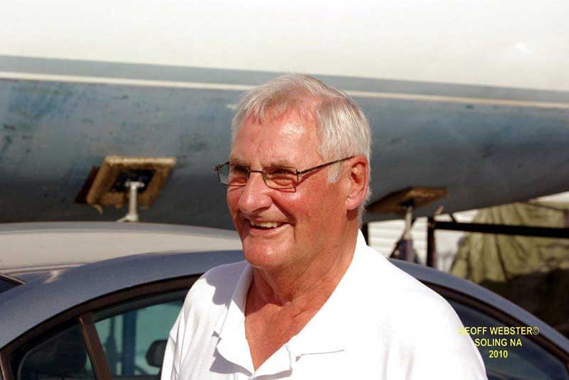 Un homme souriant portant des lunettes regarde à gauche de la photo.