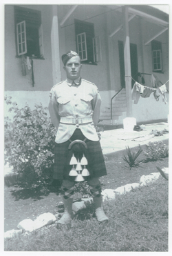 Le jeune Lawrence en kilt, debout sur l’herbe devant un immeuble.