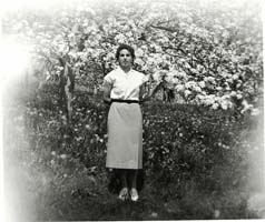 Jeune femme en jupe et chemisier debout devant des arbres.