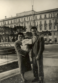 Homme et femme avec un bébé, debout devant un immeuble imposant.
