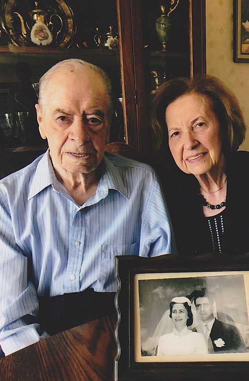 Un couple âgé assis derrière une image encadrée d’eux comme un jeune couple.