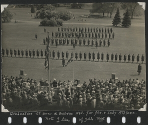 Vue aérienne d’un champ avec une large foule regardant une formation militaire.