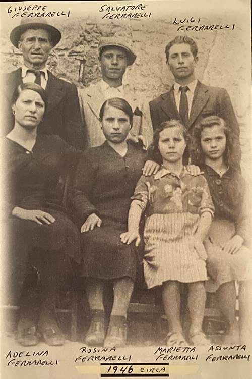 Très vieille photo de femmes assises avec des hommes debout derrière elles, toutes sans sourire.