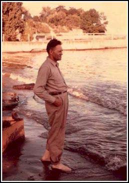 Un jeune homme est debout sur le bord de l’eau , il est pieds nus.