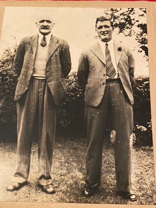 Deux hommes sont debout dans un jardin avec des arbres derrière eux.